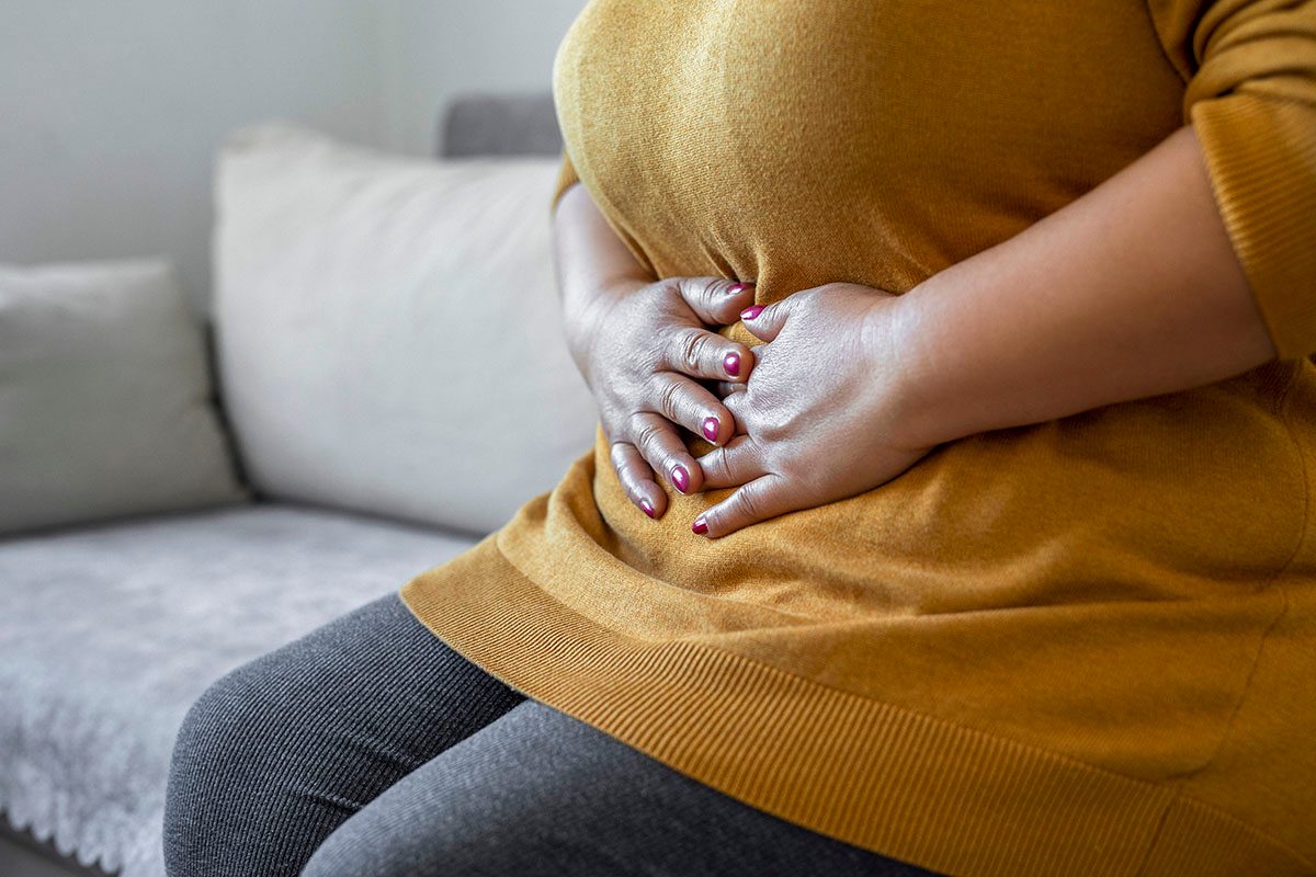 A woman has her hands on her stomach, signalling discomfort