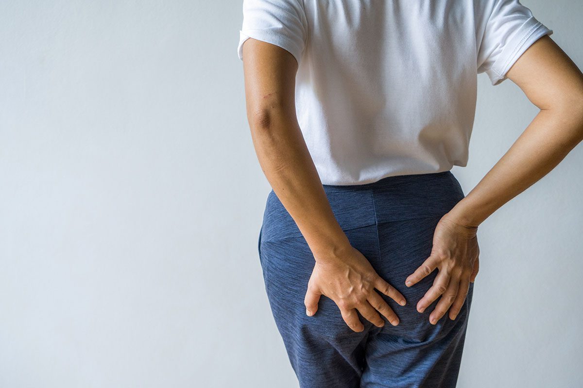 A woman stands with her back facing the camera, with her hands on her buttocks