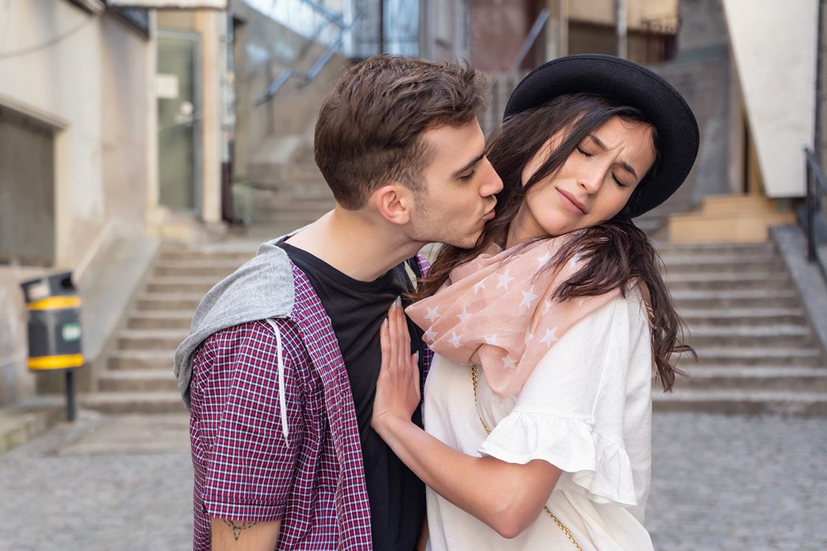 A young male is leaning in to kiss his girlfriend but she is pushing him away and frowning.