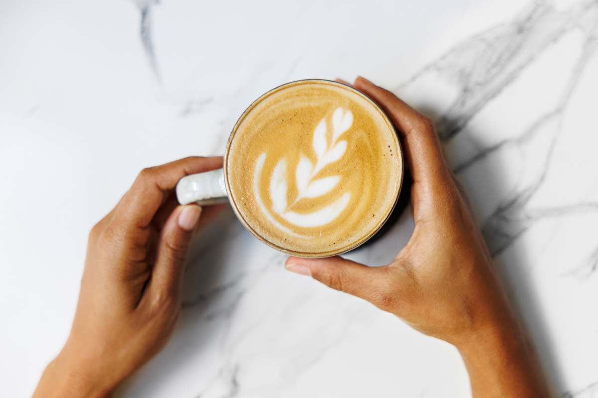 Hands hold a cup of coffee featuring latte art.