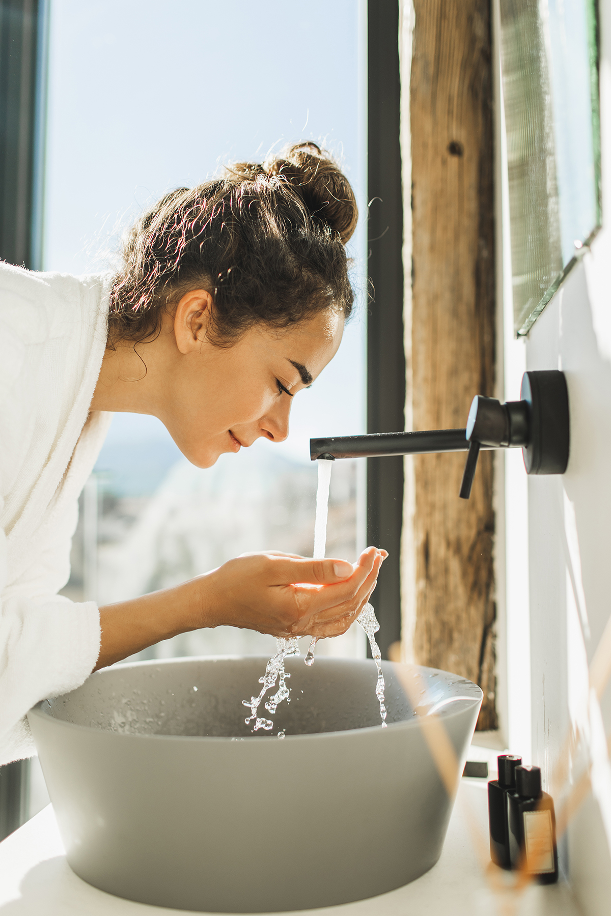 A woman washes her face over a grey stone sink.