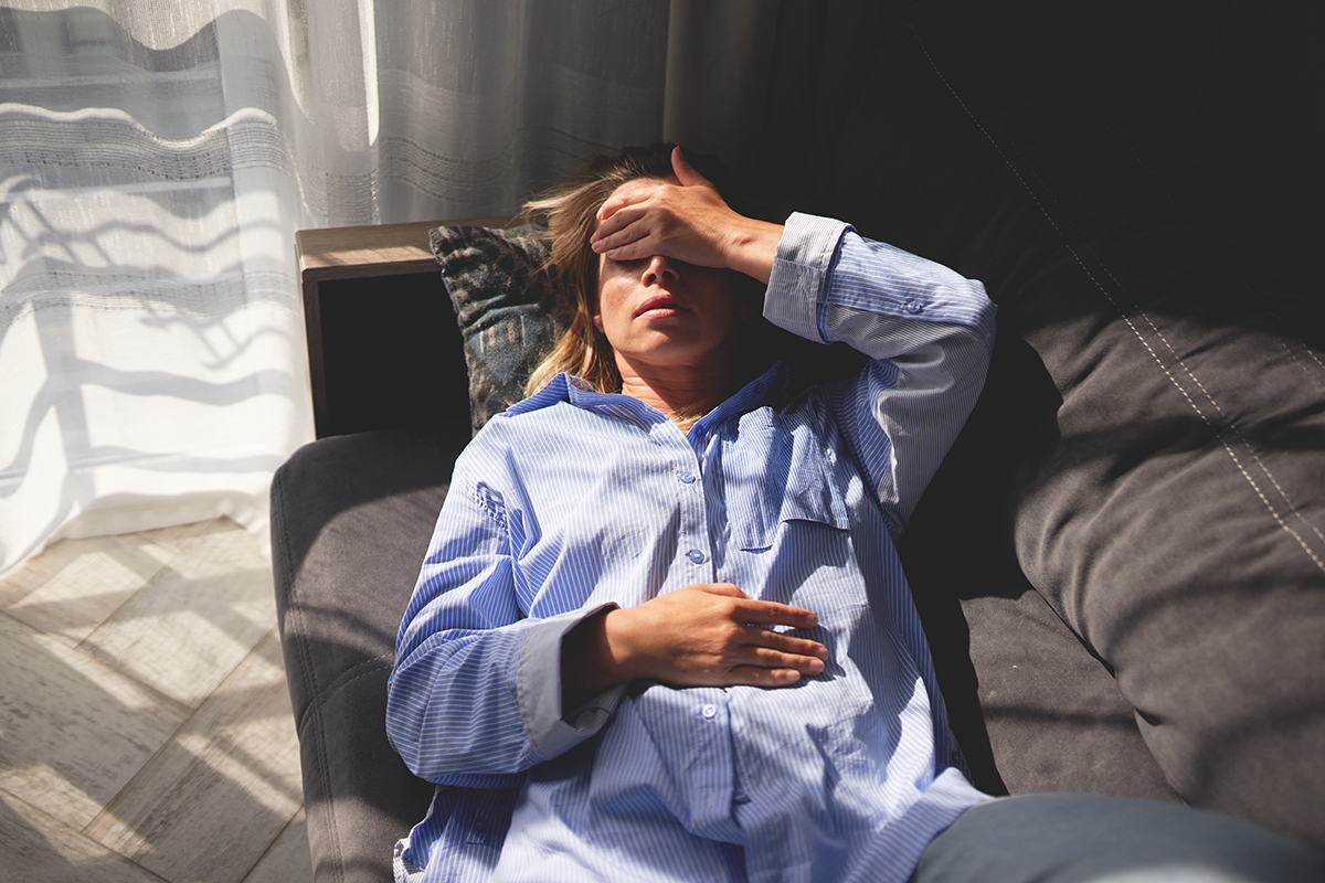 A woman lying on a sofa with her hand on her forehead