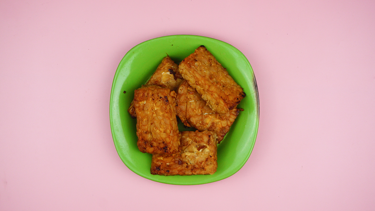 Fried tempeh on a green plate against a pink background