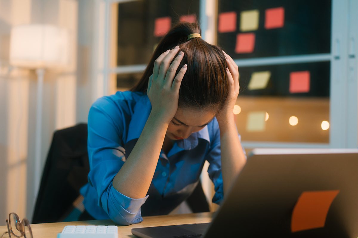A woman sitting at a desk in front of a laptop with her head in her hands