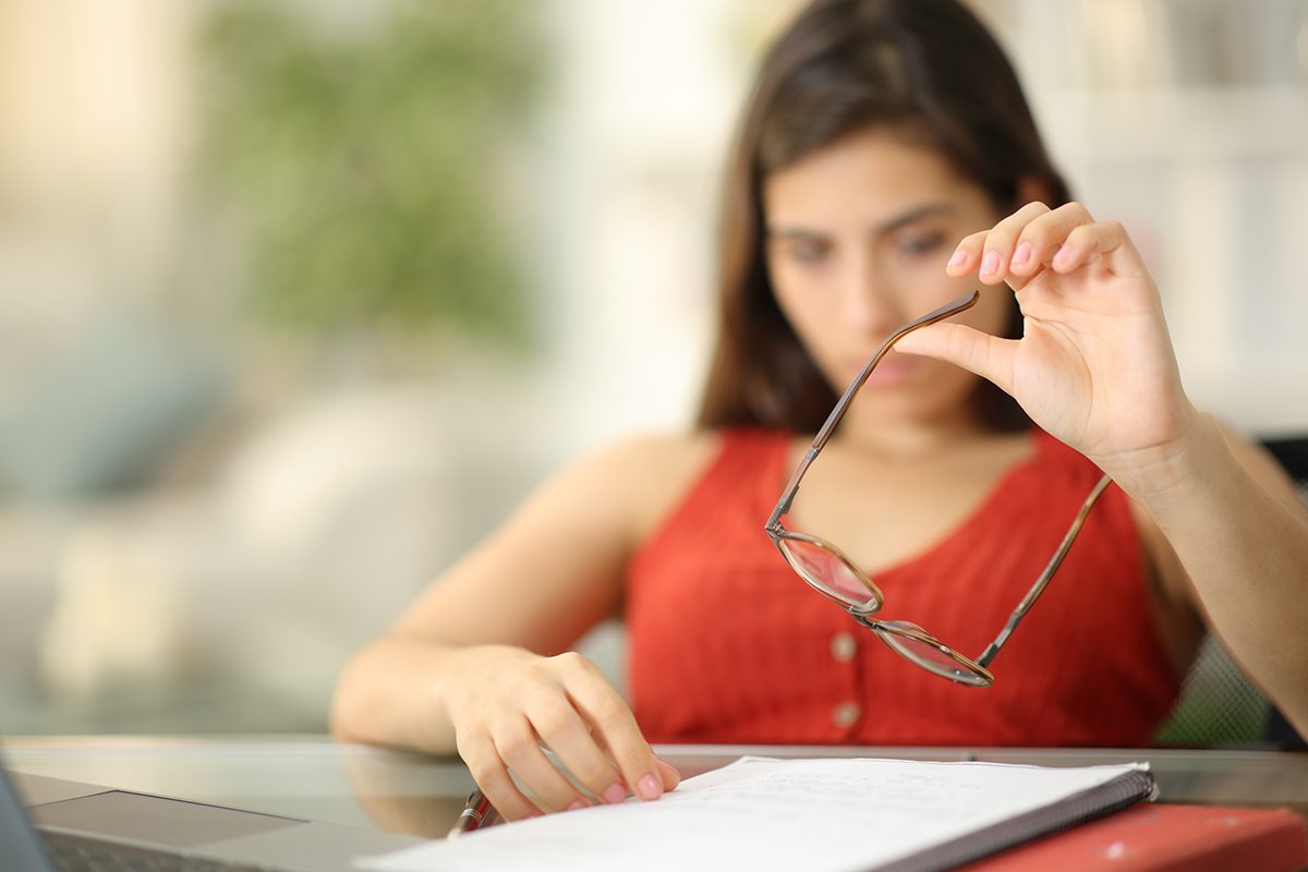 A woman is sitting at a desk playing with her glasses, appearing bored