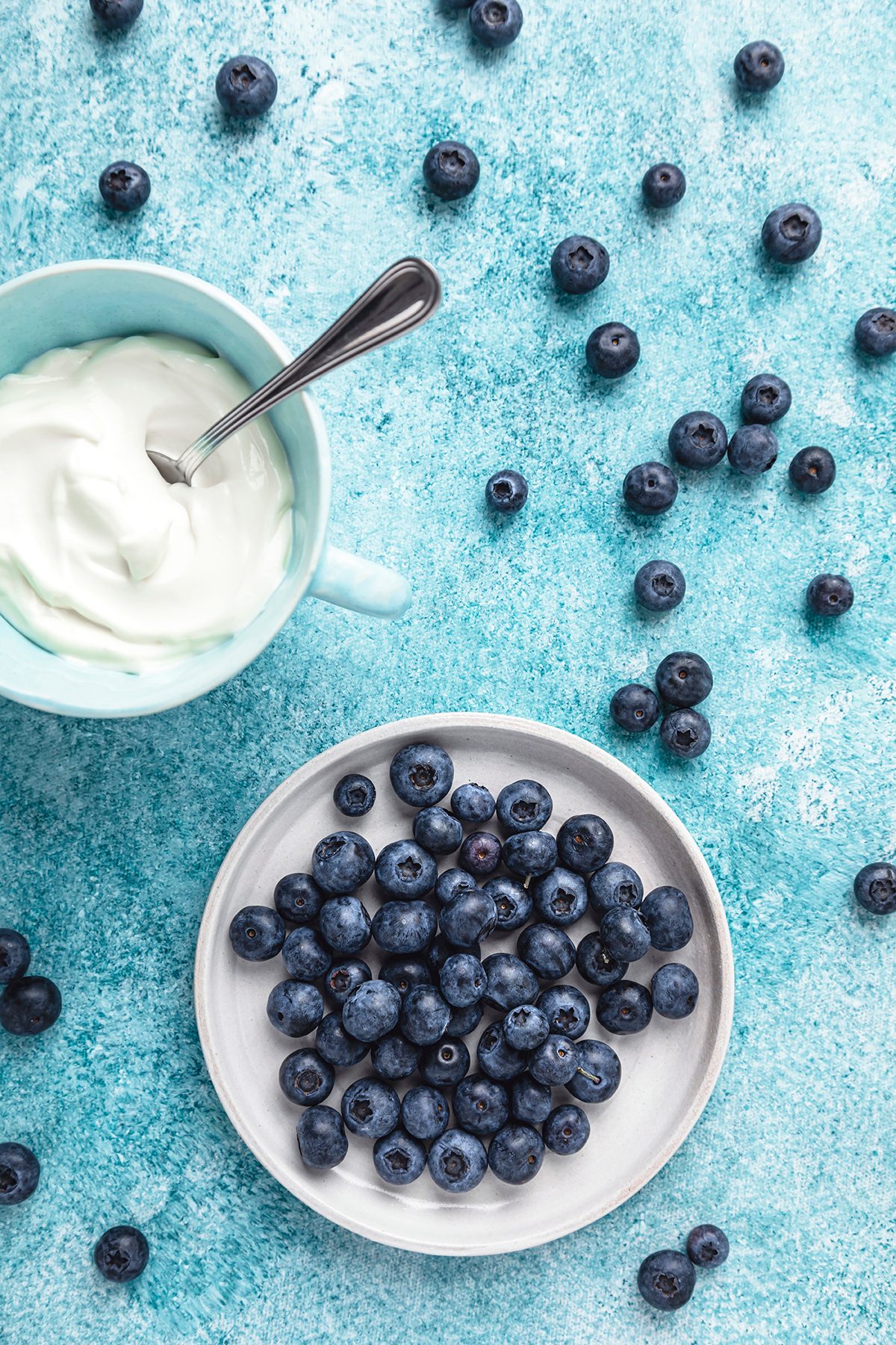 Blueberries in a bowl and yoghurt in a mug on a blue background.