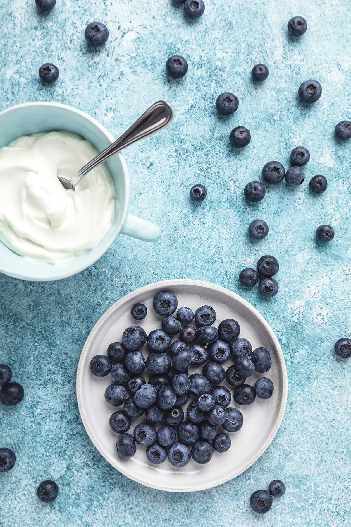 Blueberries in a bowl and yoghurt in a mug on a blue background.
