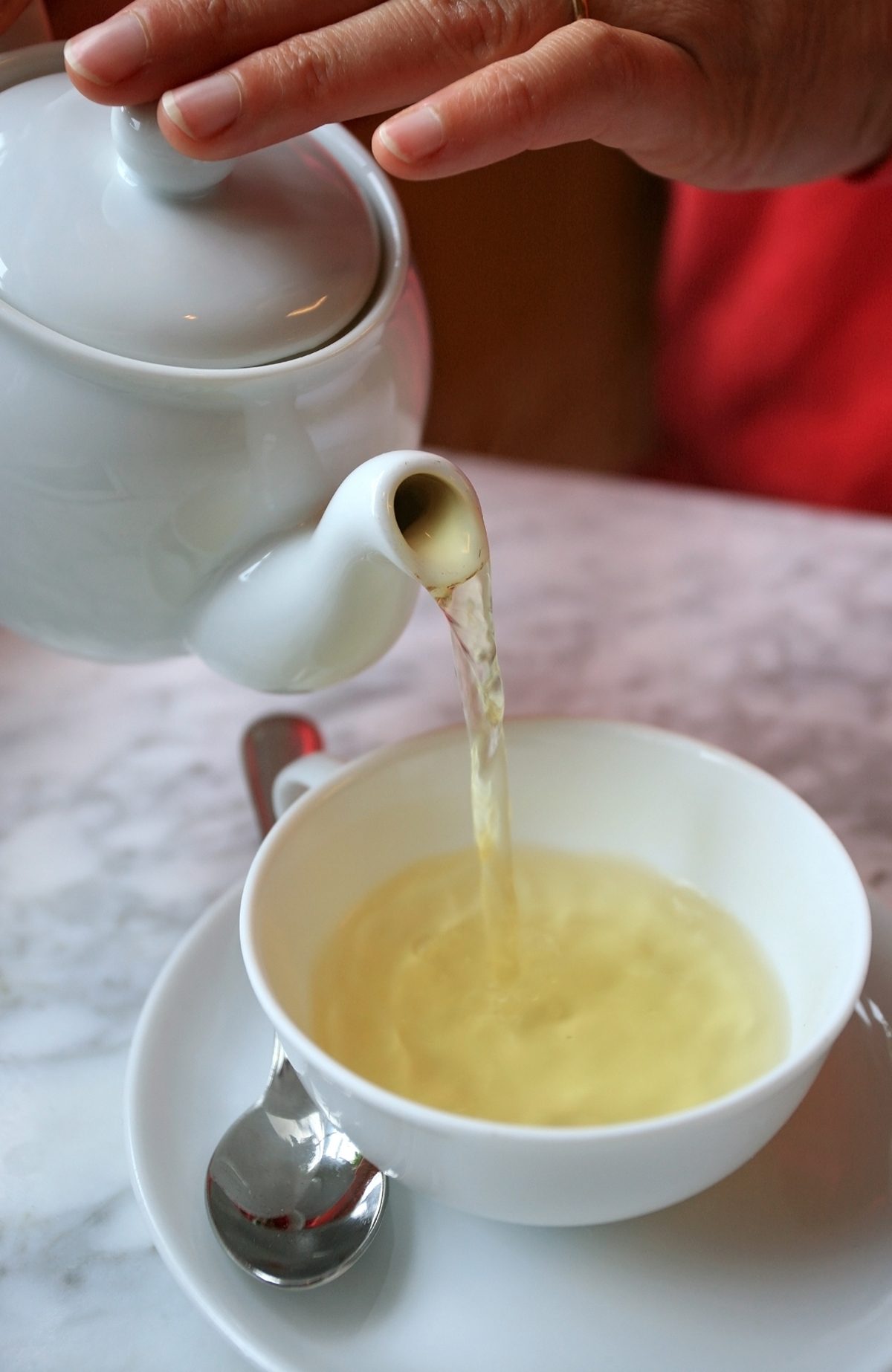 Woman pouring green tea from the tea pot into a cup.