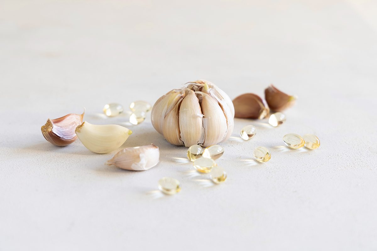 A photo of capsules near a whole bulb of garlic and cloves on a white table.