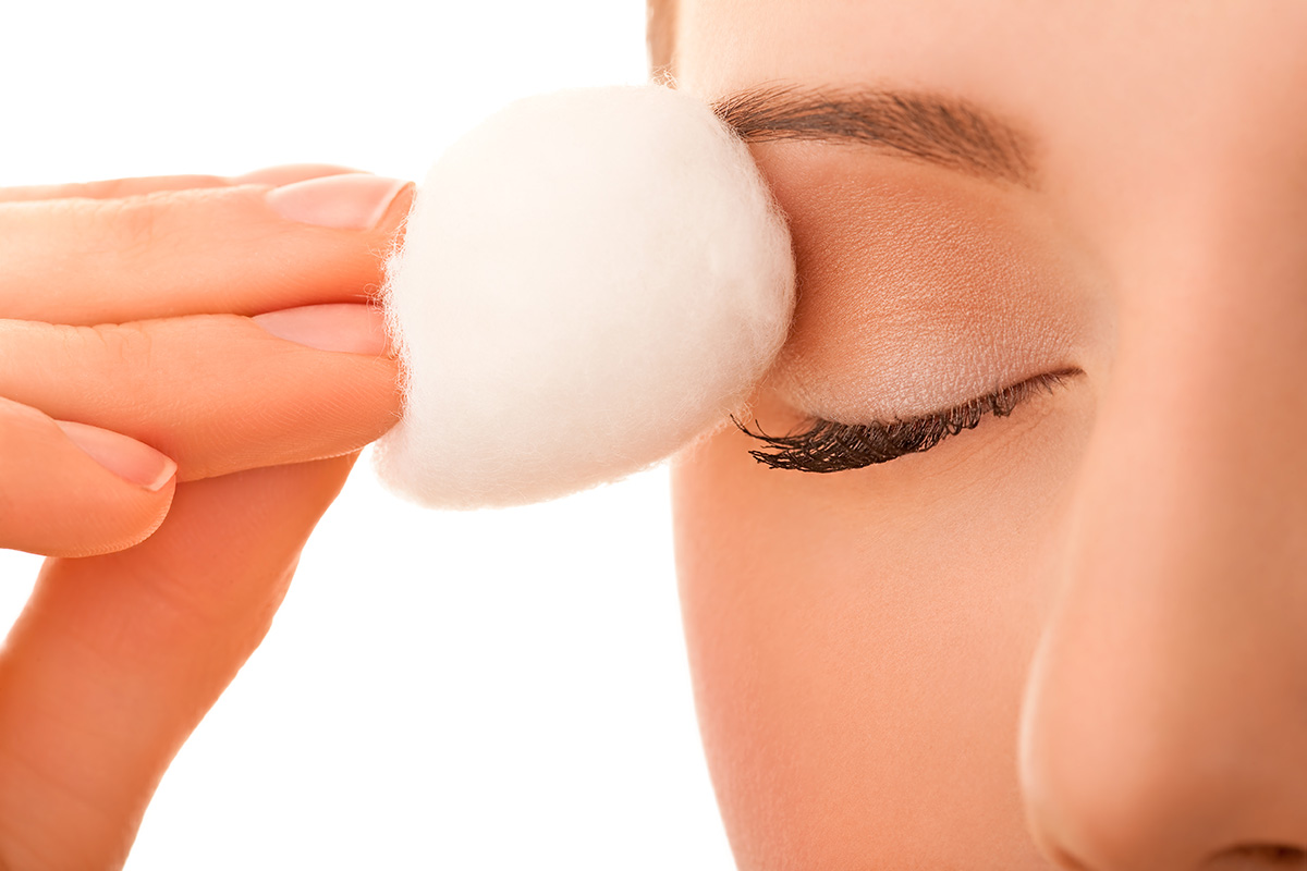 A woman removing eye makeup with a cotton ball