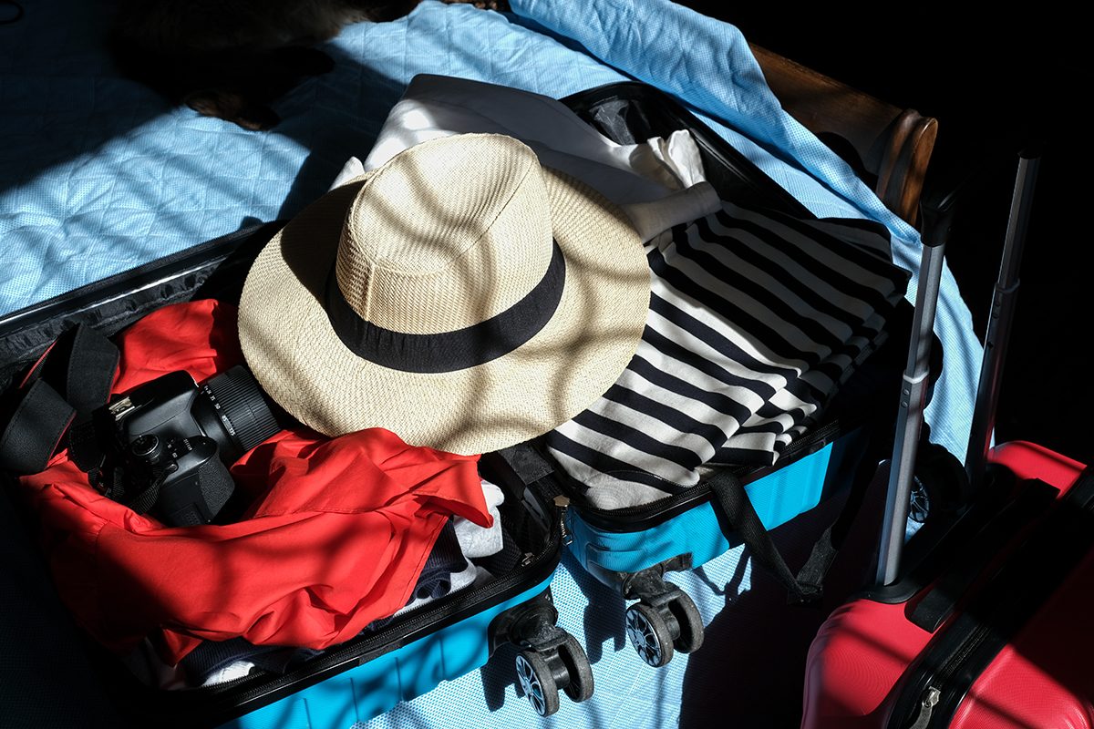 A suitcase filled with clothes, a sunhat and a camera is open on a bed