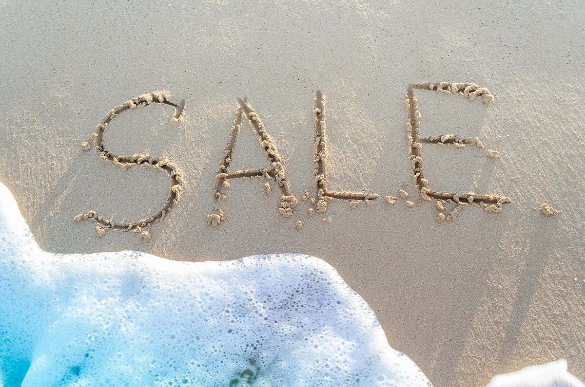 The word "SALE" is written in sand next to a small wave
