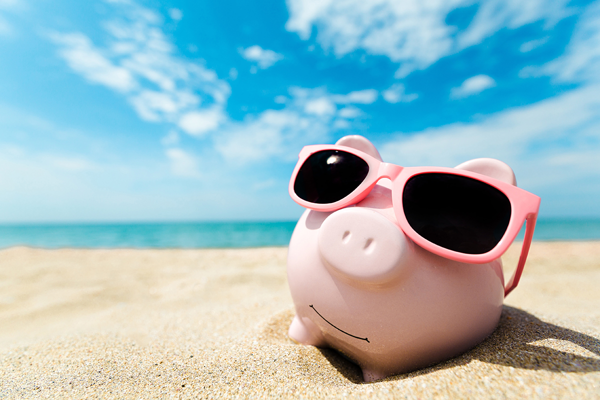 A piggy bank wearing sunglasses on a sandy beach