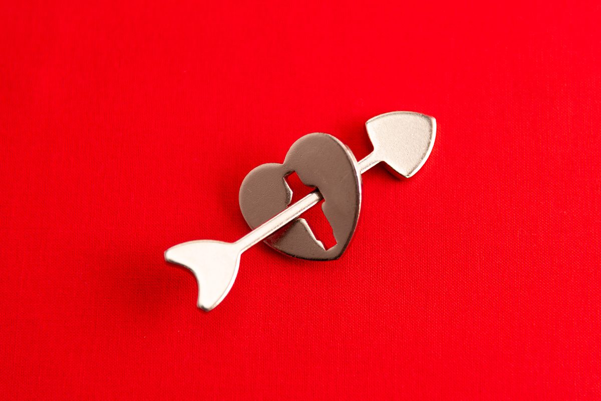 A heart-shaped metal keyhole with an arrow through it against a red background