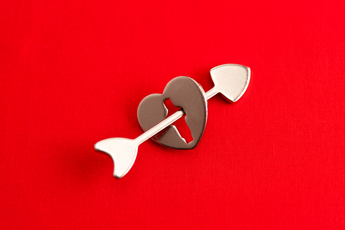 A heart-shaped metal keyhole with an arrow through it against a red background