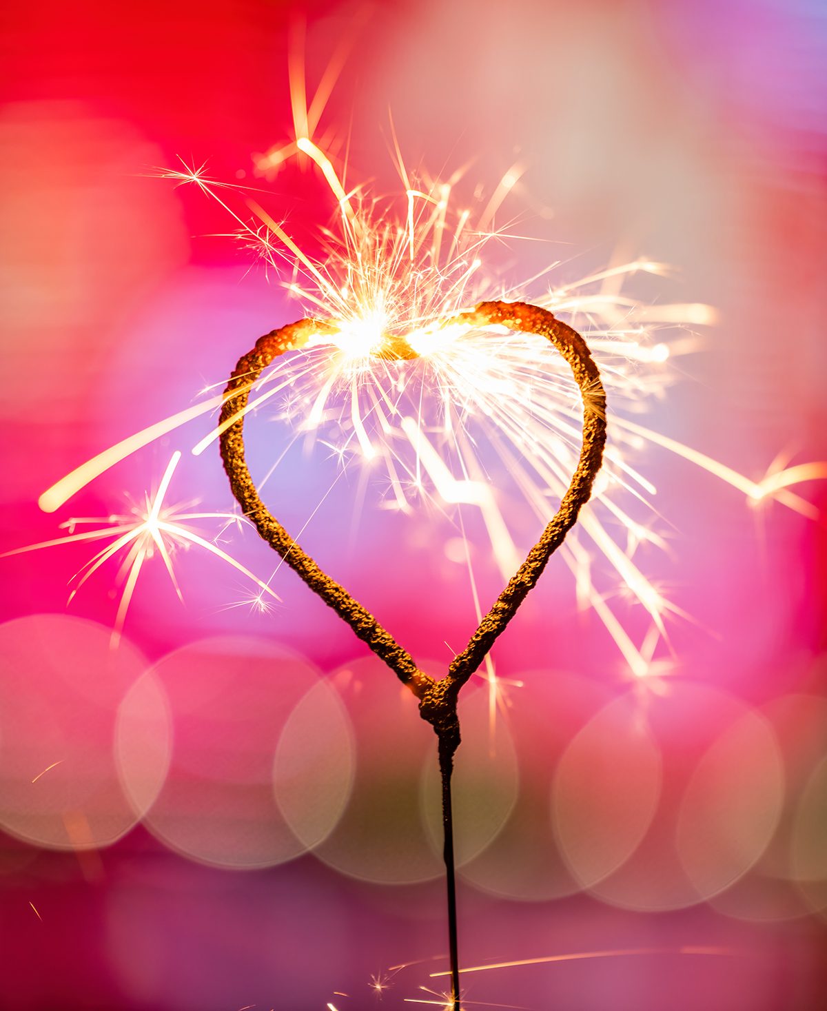 A heart-shaped sparkler is burning against a blurred red background