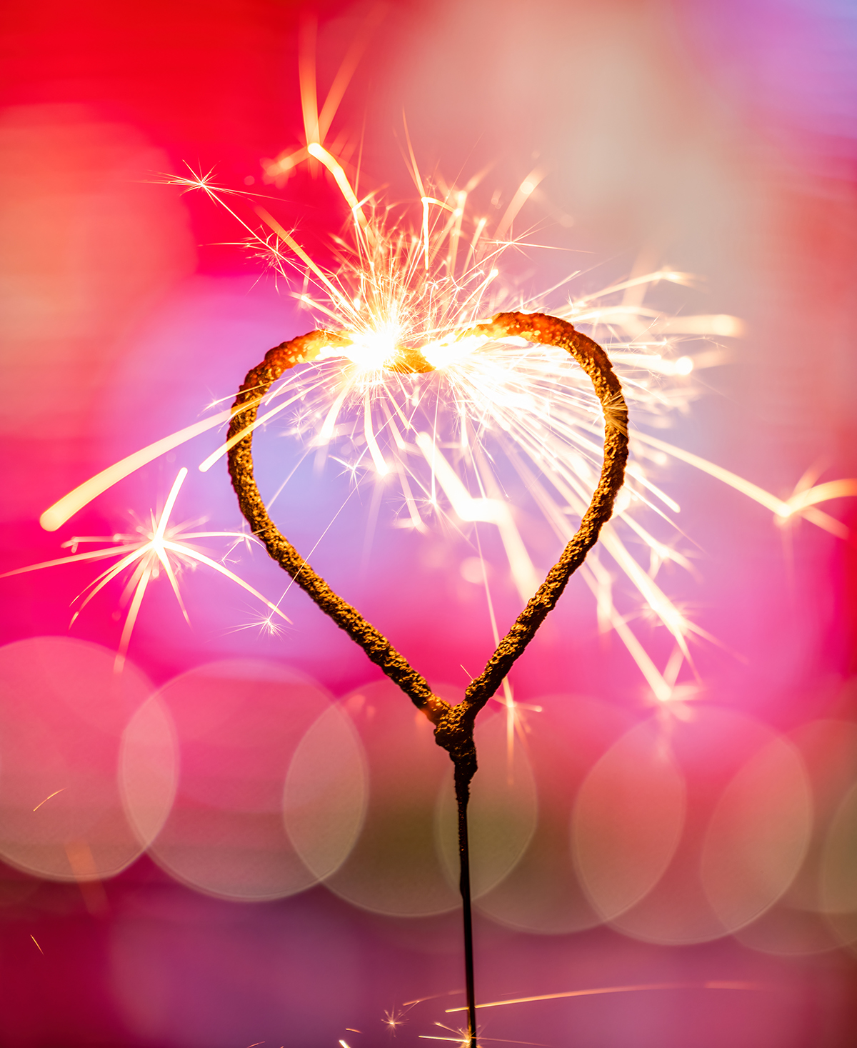 A heart-shaped sparkler is burning against a blurred red background