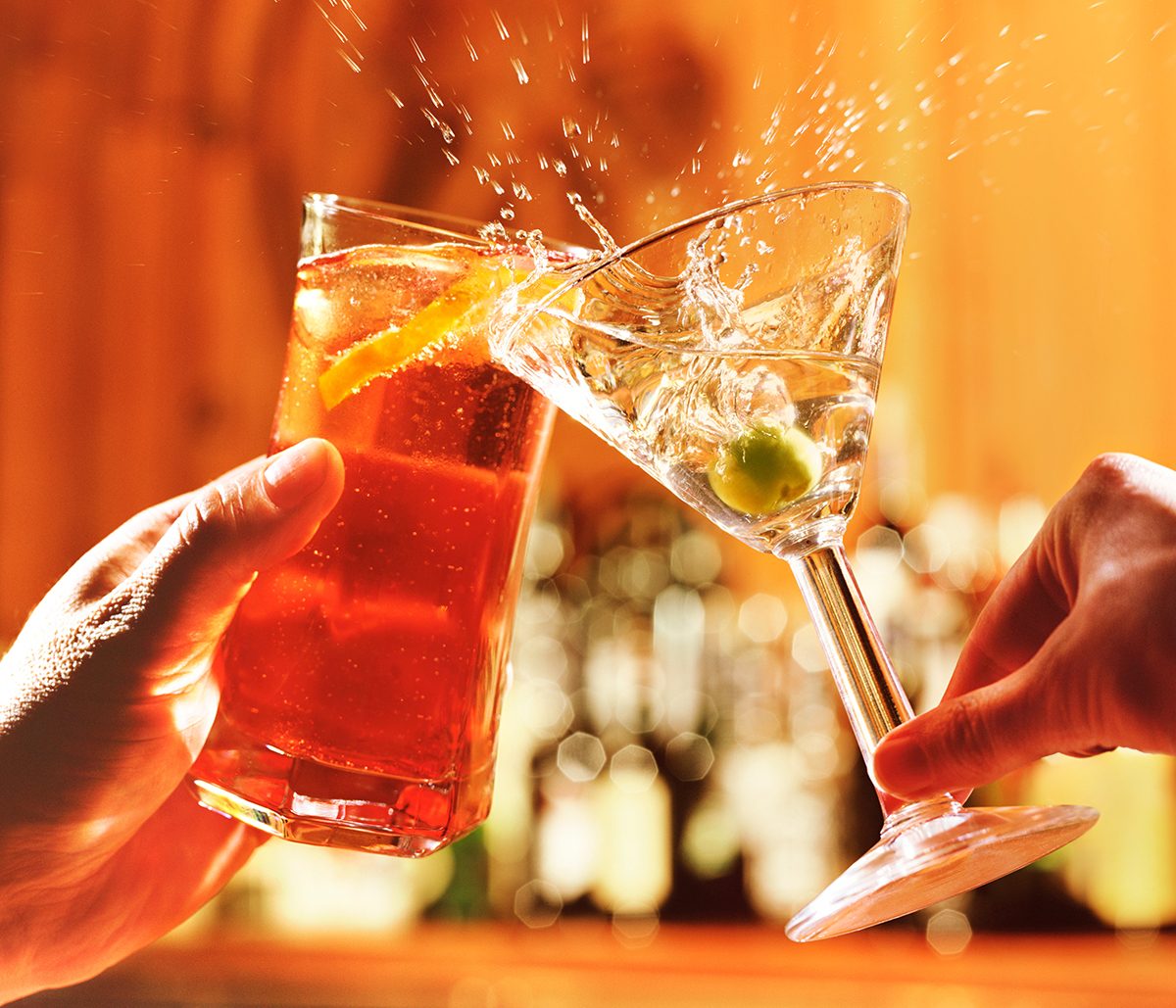 Two hands clink a tall cocktail glass and a martini glass