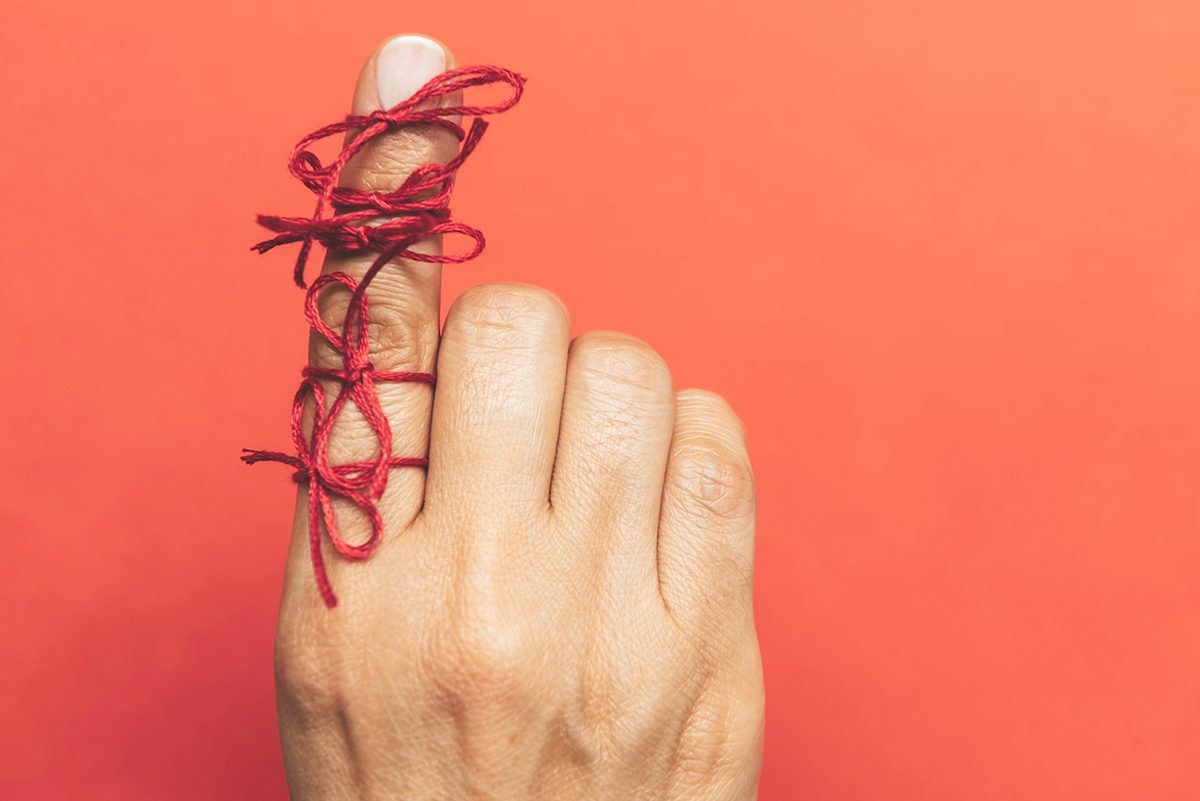 A hand with red string tied around the index finger, against an orange background