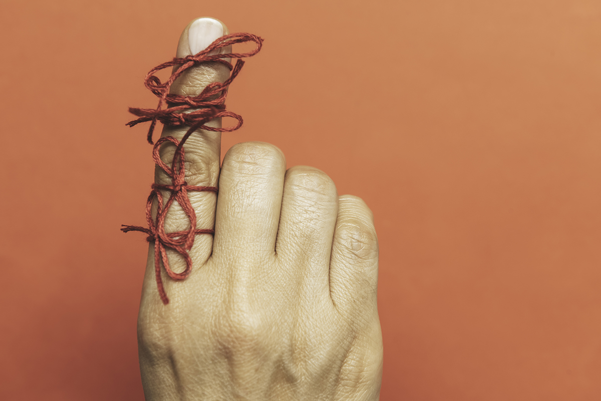 A hand with red string tied around the index finger, against an orange background