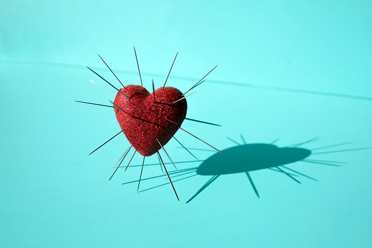 A 3D red heart with needles sticking out of it against a blue background
