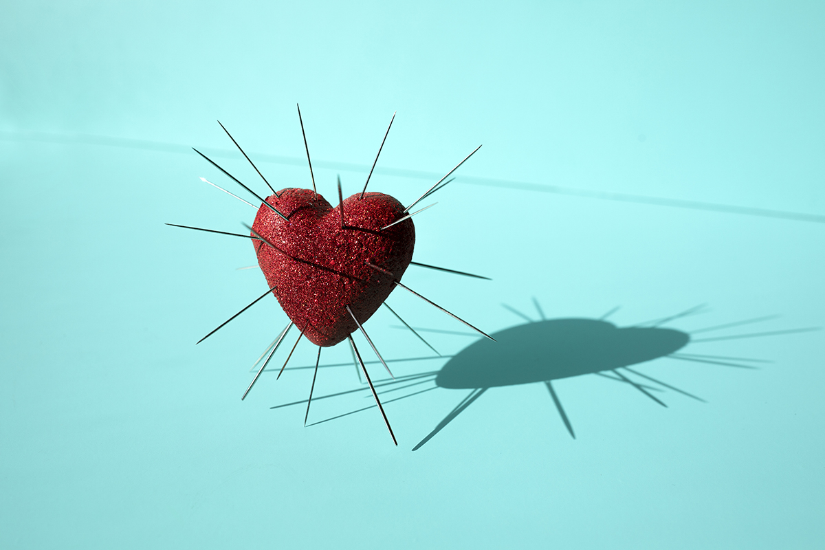 A 3D red heart with needles sticking out of it against a blue background