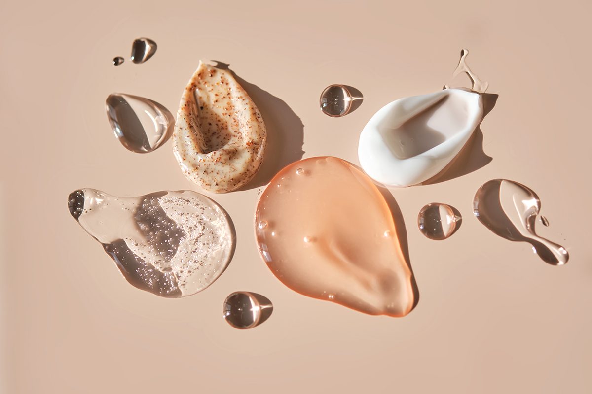 Swatches of different cosmetic products, including creams and gels, on a beige background