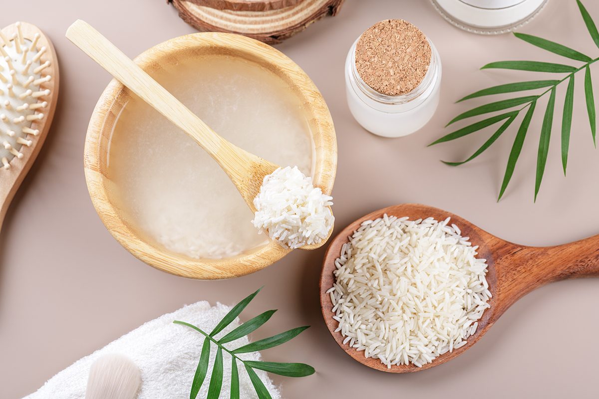 A wooden bowl of rice water and a wooden spoon with rice on a beige background