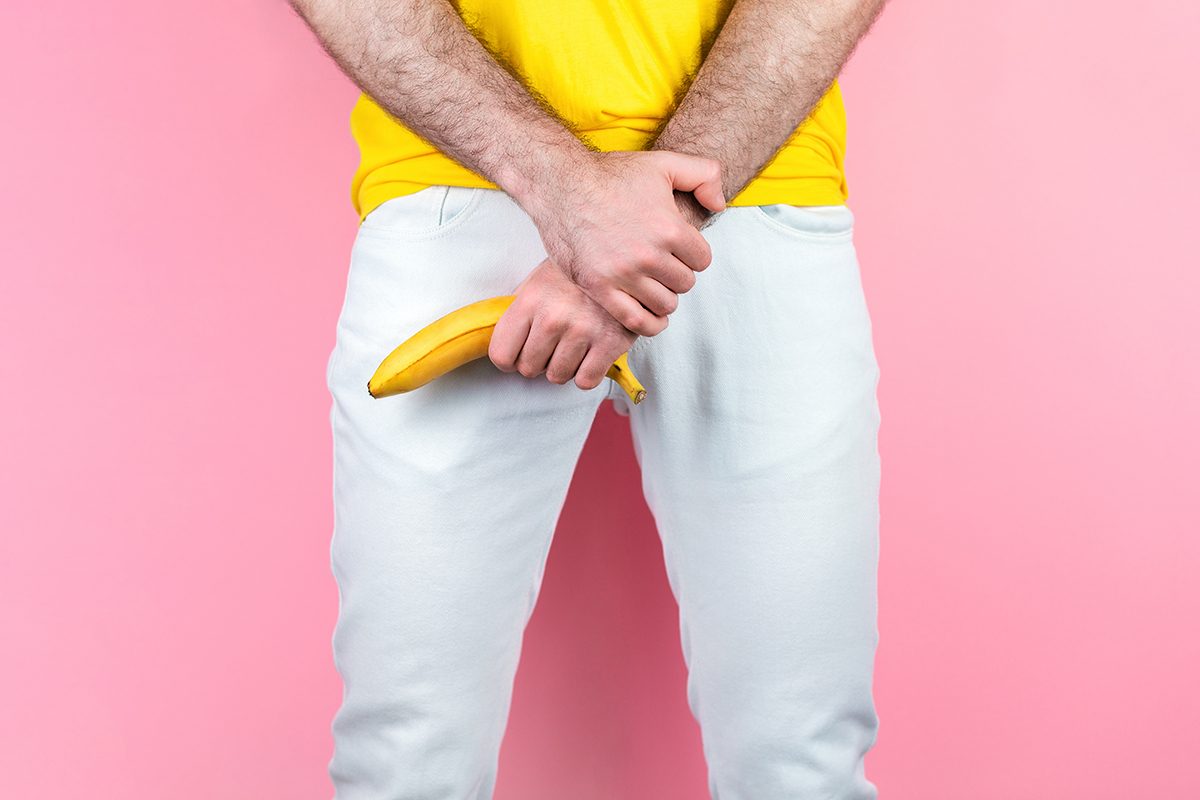 A man holding a banana is standing in front of a pink background