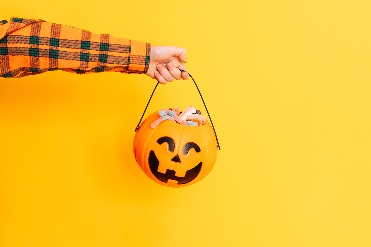 A hand holding a treat bucket in the shape of a pumpkin against a yellow background