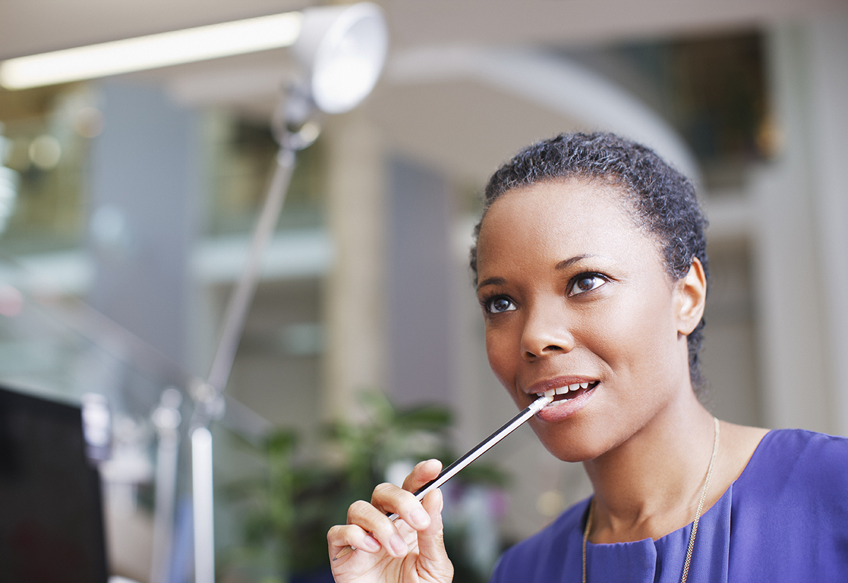 A woman is biting on the end of a pencil in an office