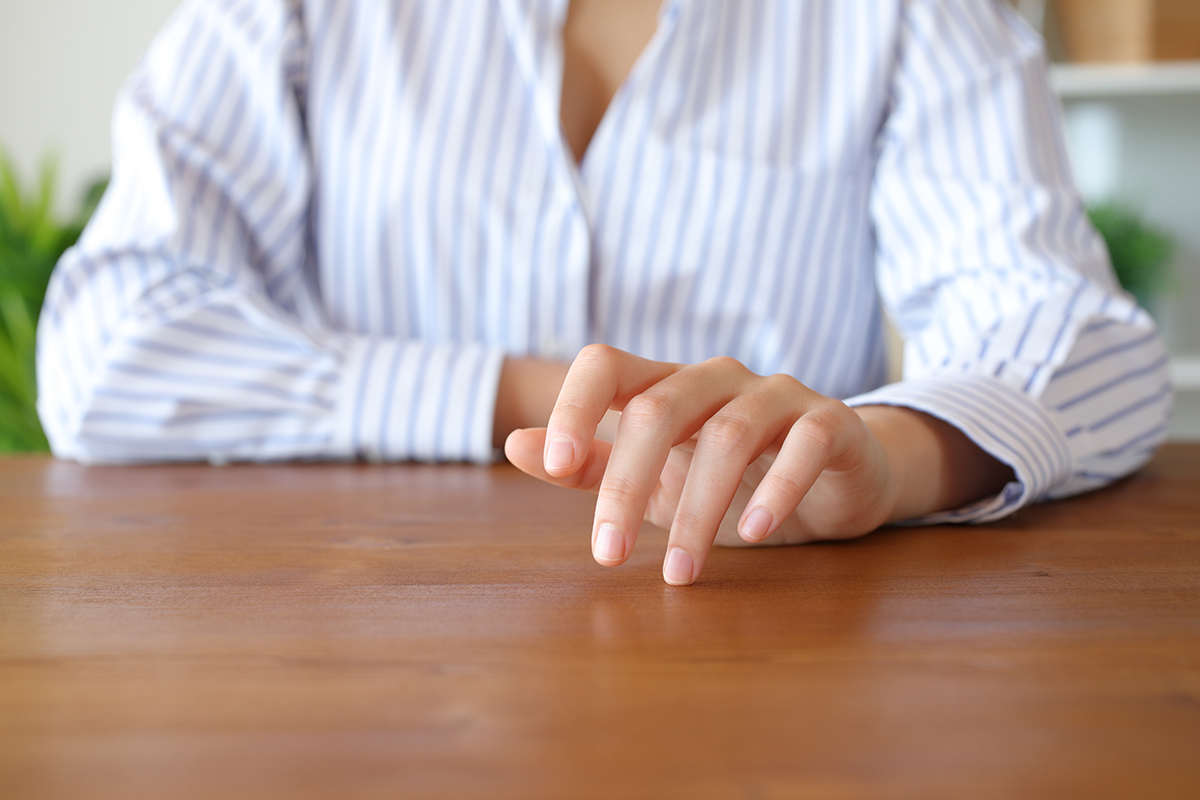 A woman tapping her fingers on a wooden table