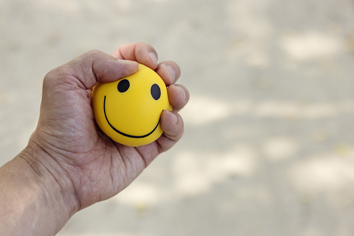A hand squeezing a stress ball featuring a smiley face