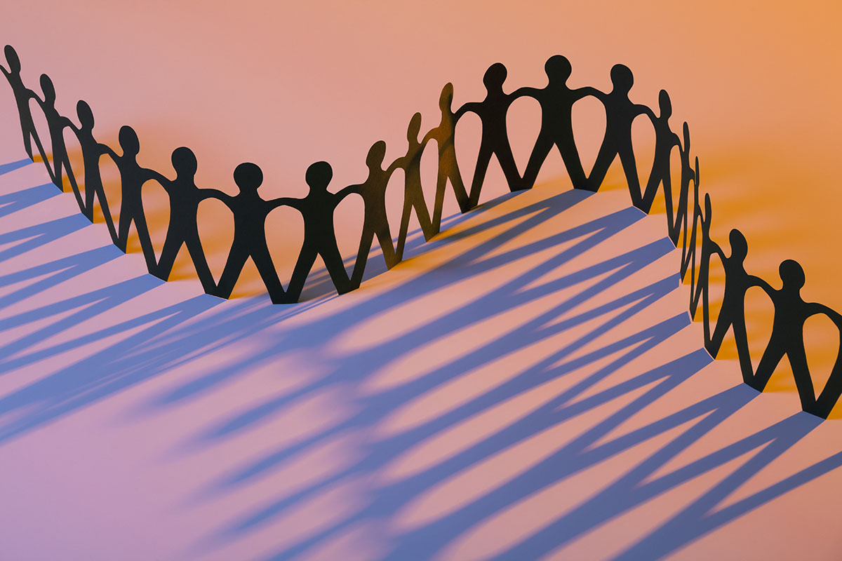 A paper doll chain casting a shadow on an orange background