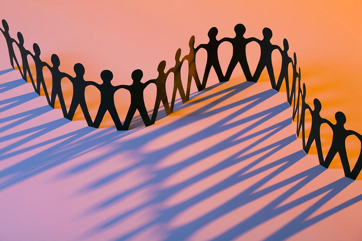 A paper doll chain casting a shadow on an orange background