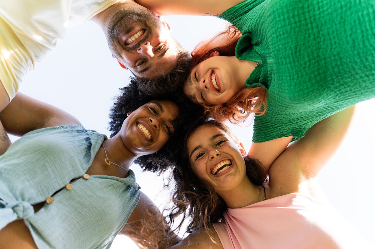 A low-angle shot of four friends embracing and smiling at the camera