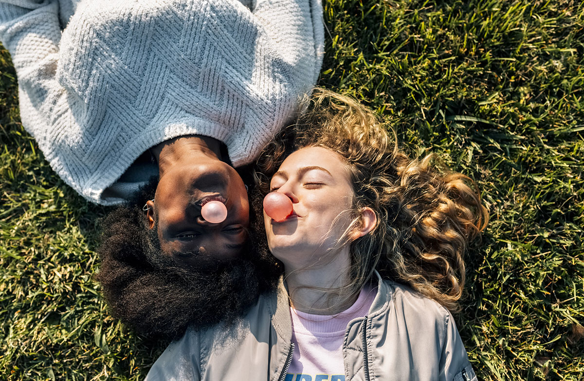 Two women lying on the grass blowing bubblegum bubbles