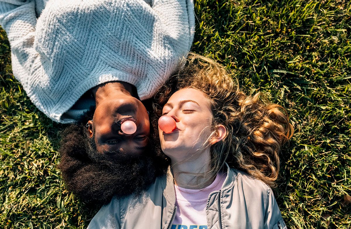 Two women lying on the grass blowing bubblegum bubbles