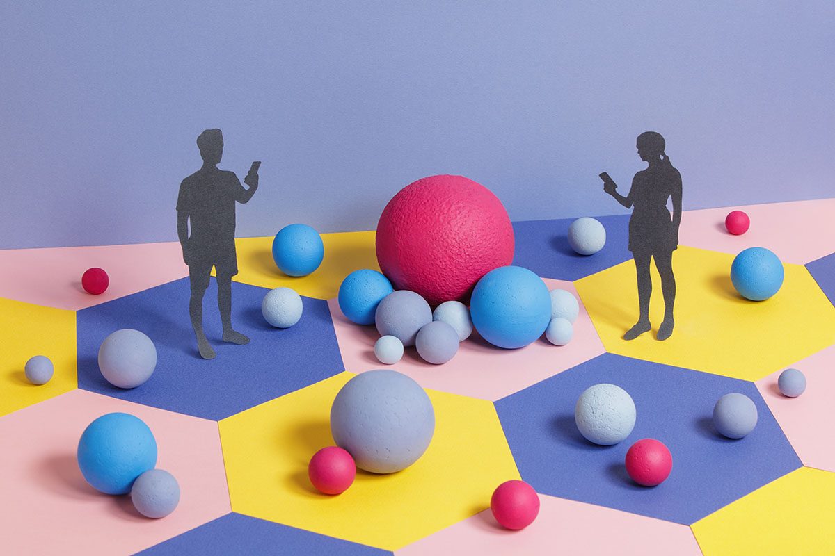Male and female figures made from paper holding mobile phones are positioned on a colourful background surrounded by different-sized balls