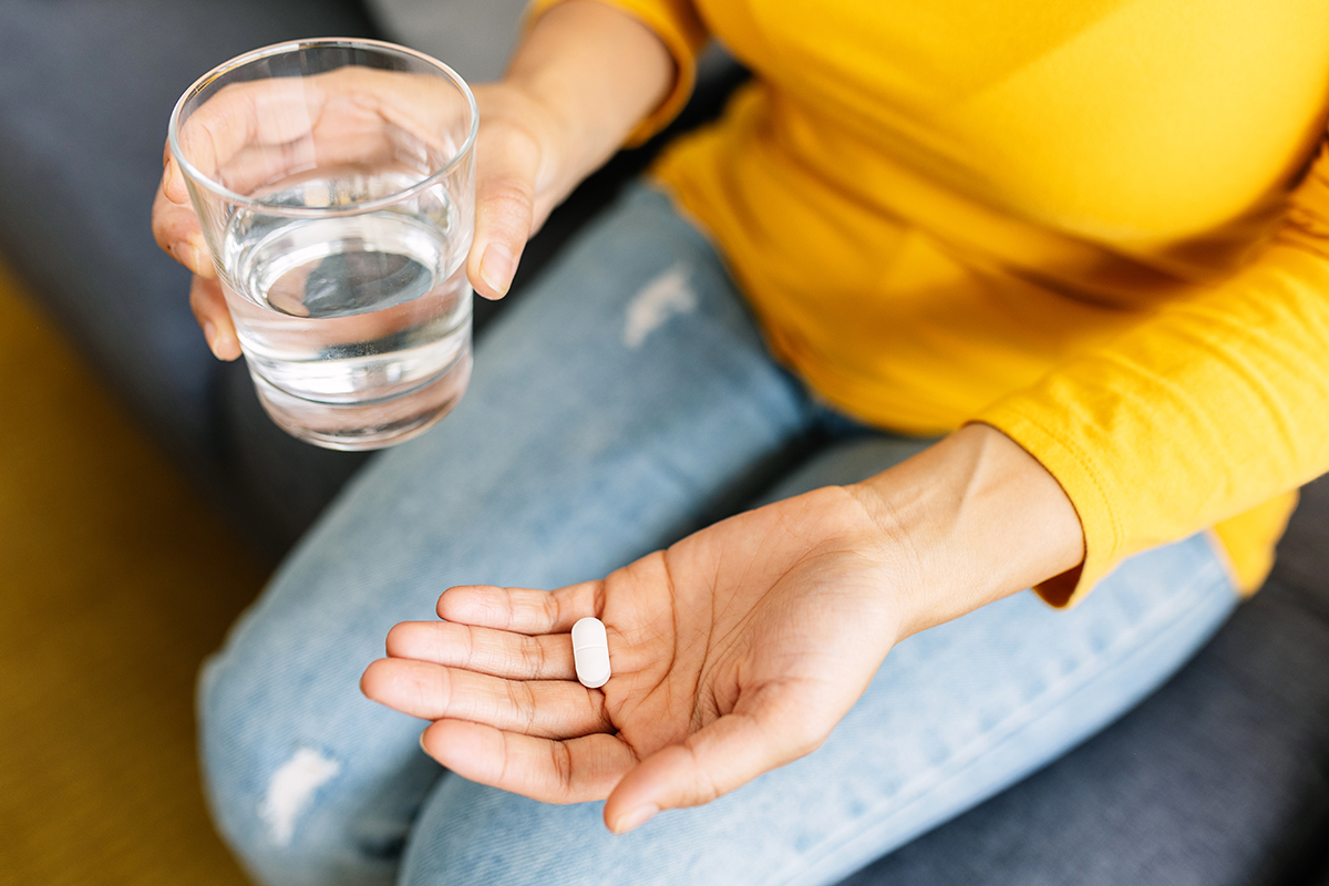 A woman holds a glass of water in one hand and a white tablet in the other.