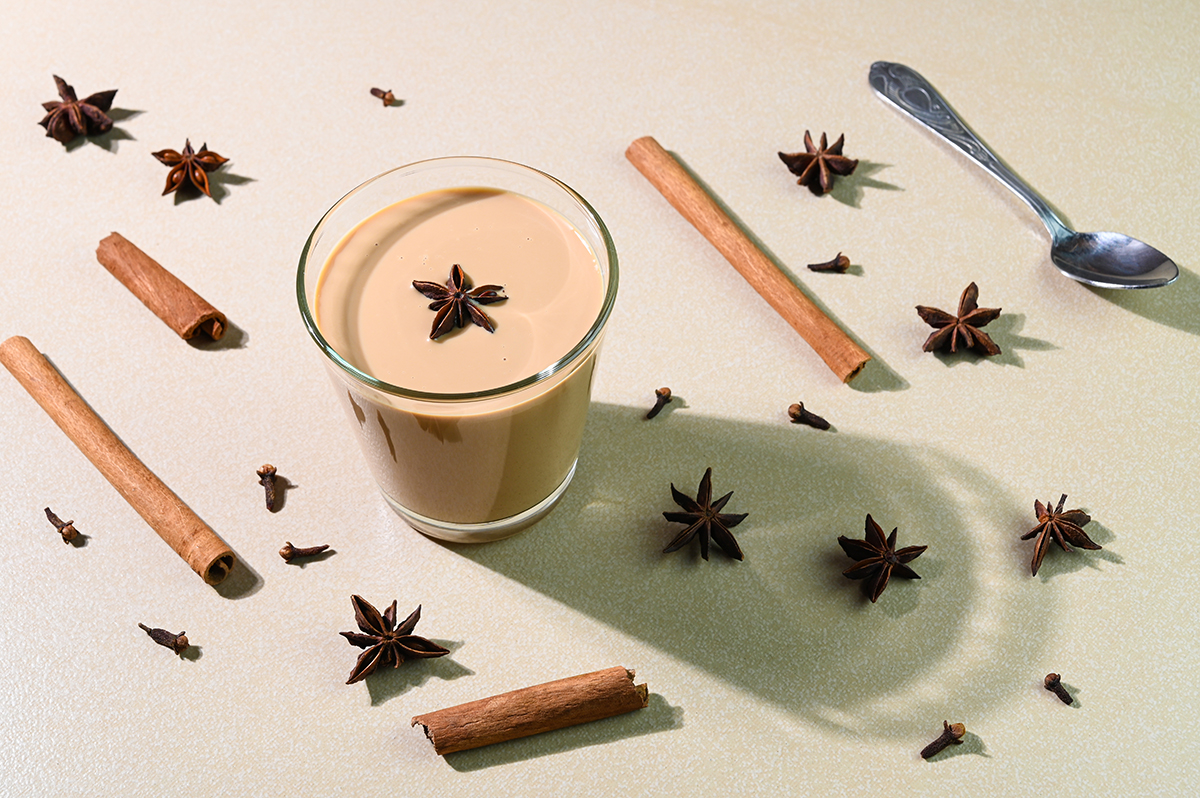 A glass cup of masala tea surrounded by cinnamon sticks and star anise.