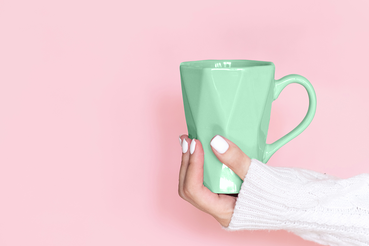 A hand holds a green mug in front of a pink background.