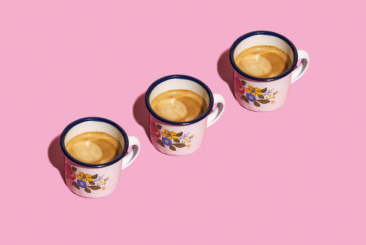 Three cups of coffee are arranged in a diagonal line on a pink background.