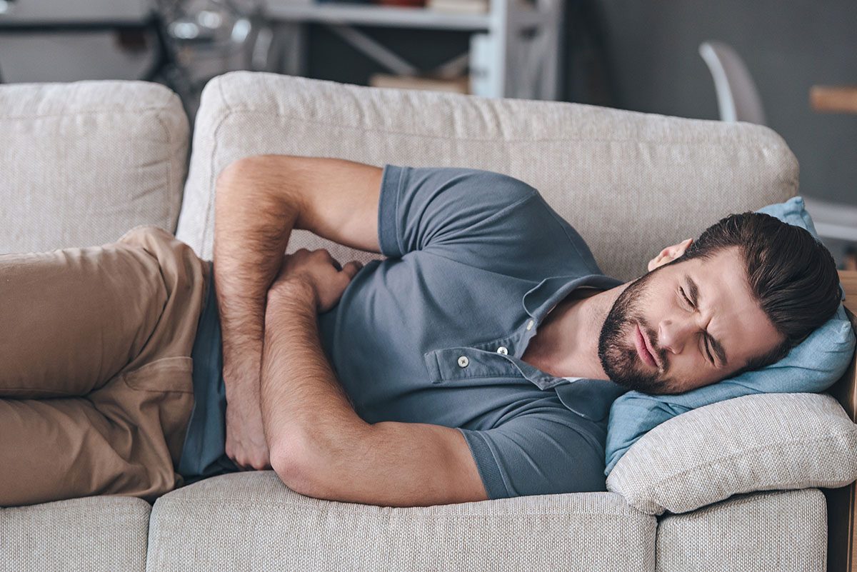A man lying on a sofa, holding his stomach as he experiences abdominal pain
