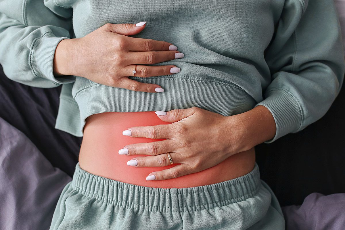 A close-up of a woman's hands resting on her abdomen, which is highlighted red to indicate pain
