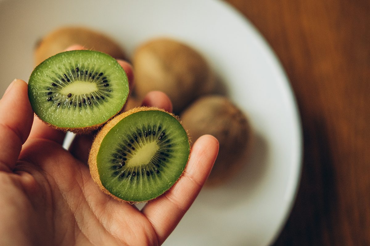 A hand holds two halves of kiwi