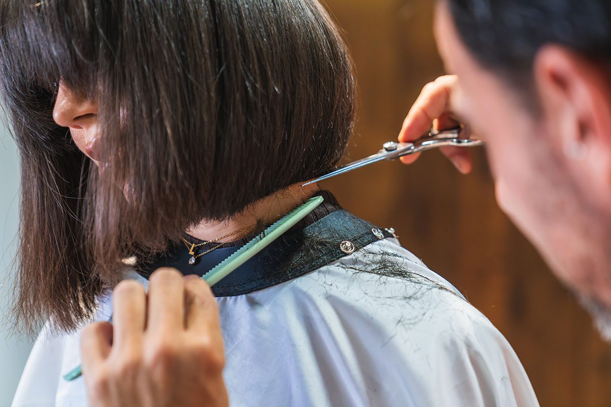 A hair stylist is trimming a woman's hair to bob length