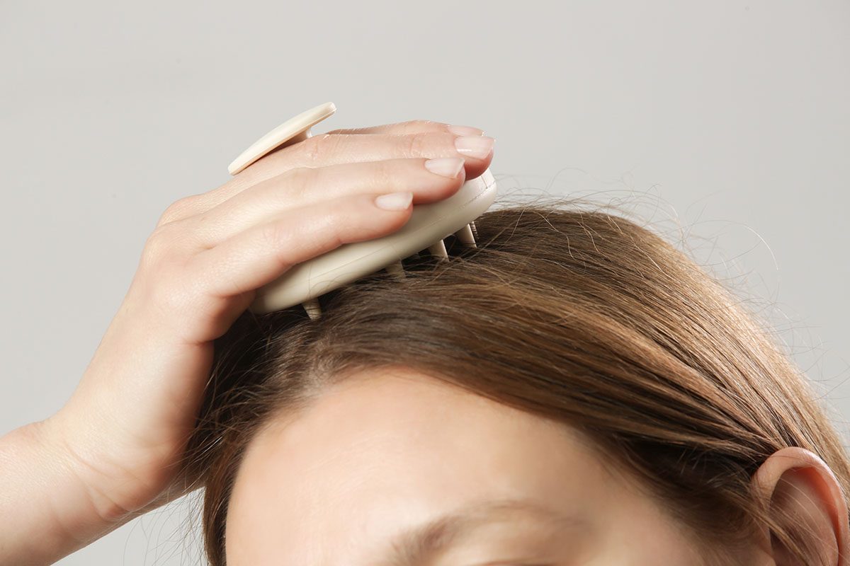 A woman using a scalp massager on her scalp 