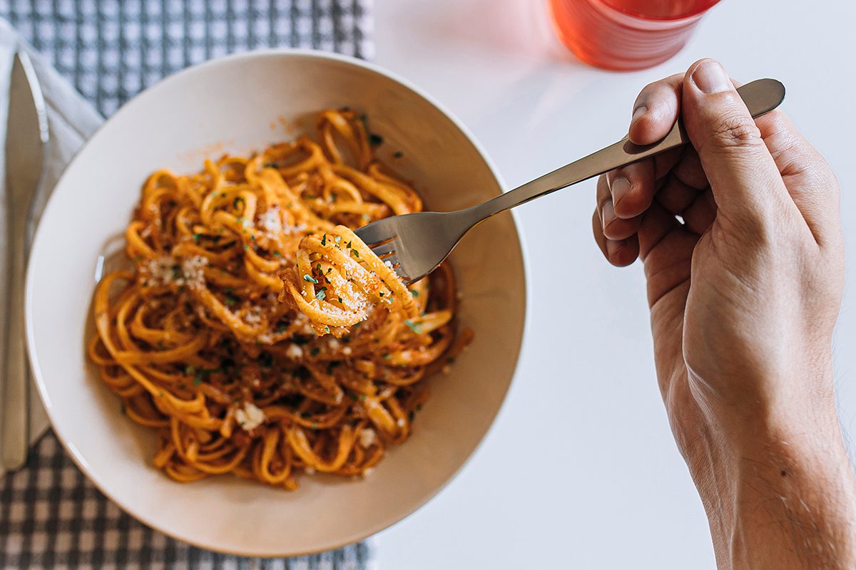 A hand is twirling a forkful of spaghetti in a bowl filled with rich, saucy pasta.