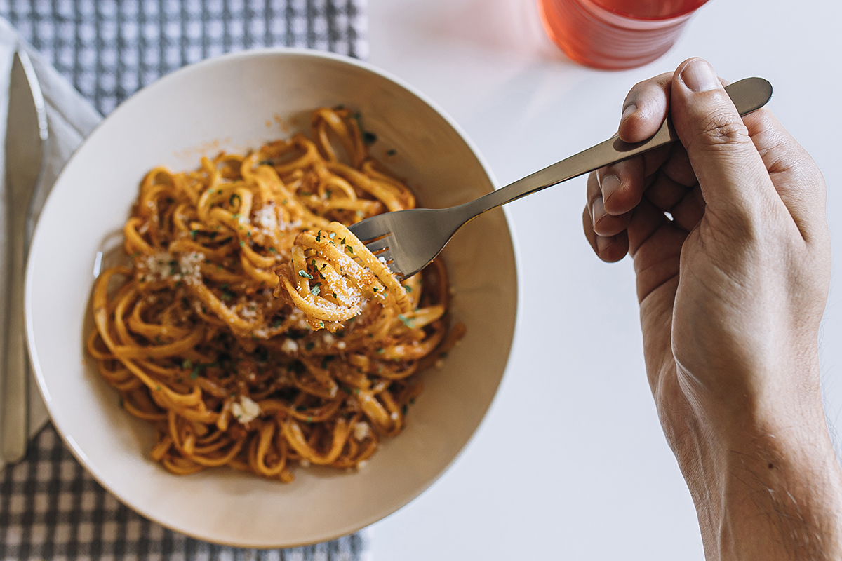 A hand is twirling a forkful of spaghetti in a bowl filled with rich, saucy pasta.